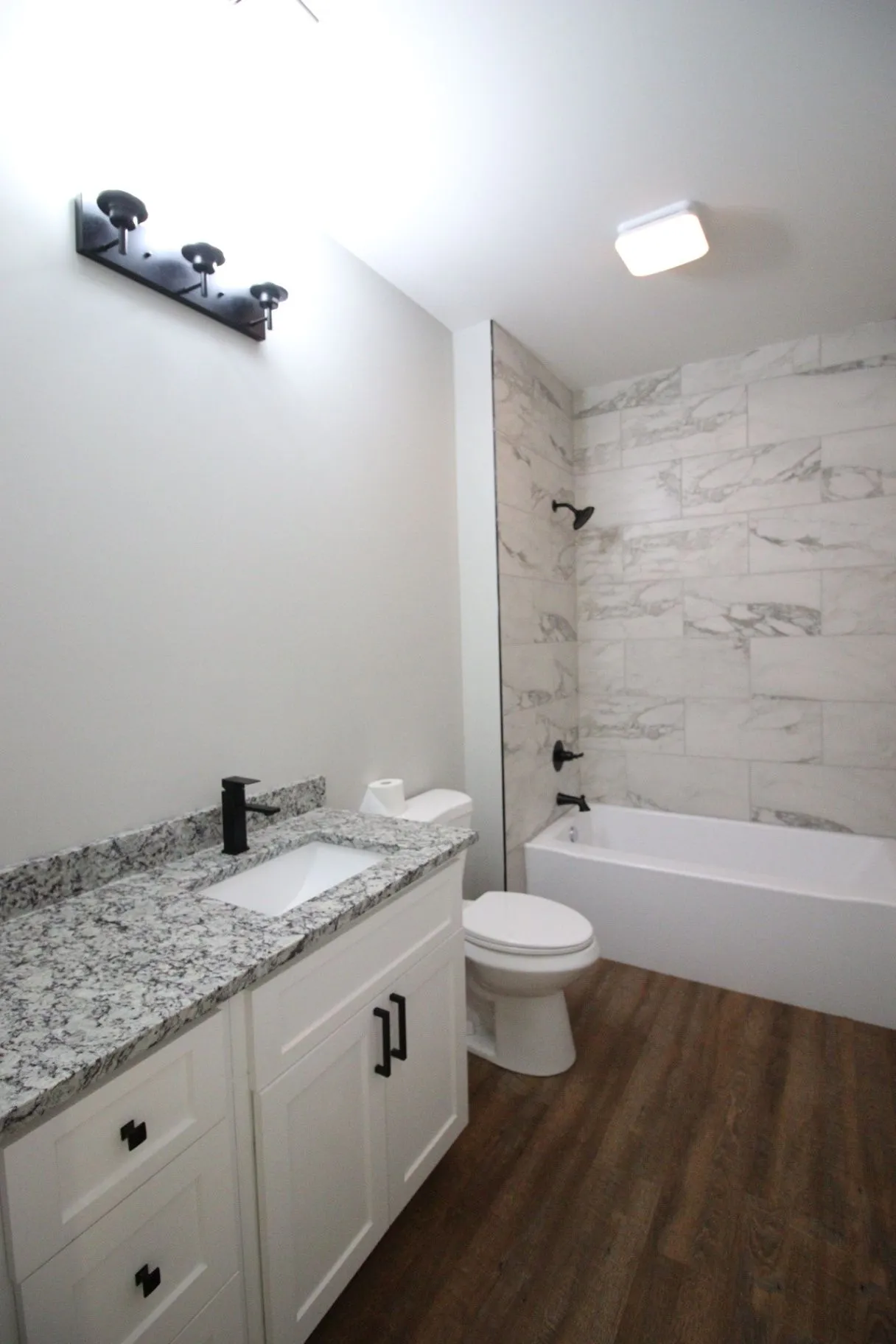 Completed JP2 New Construction bathroom with a tiled tub surround, vanity, and recessed lighting